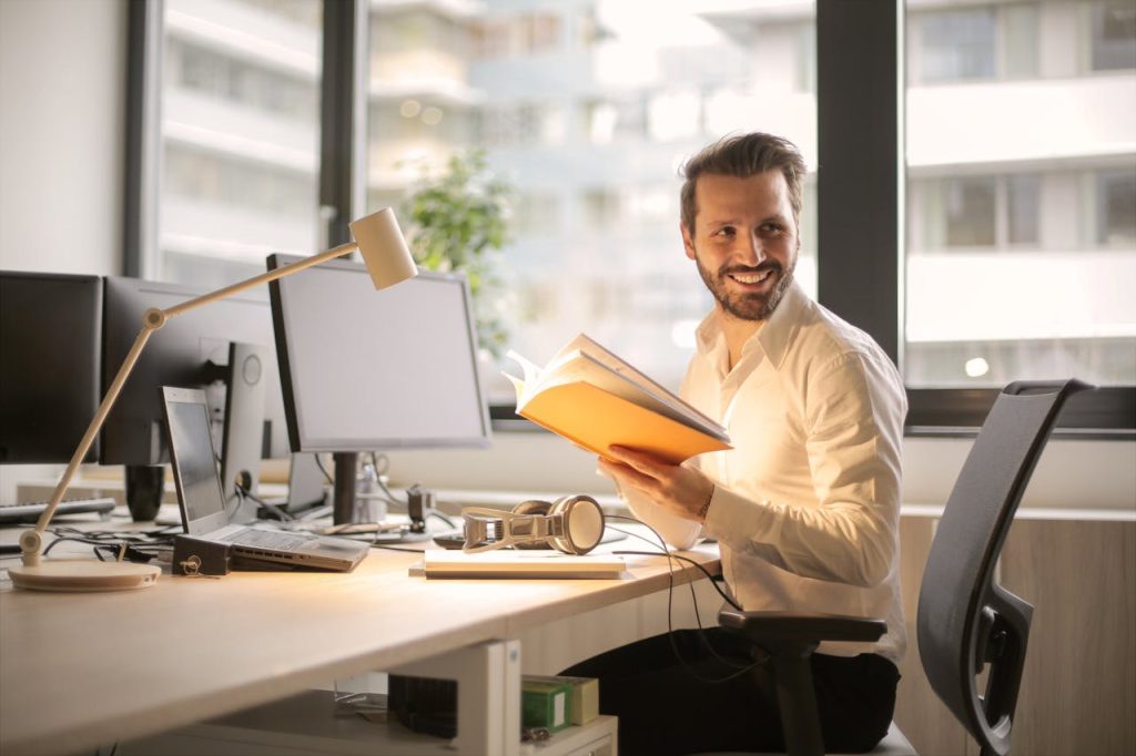 Man smiling sitting in front of a desk holding a book