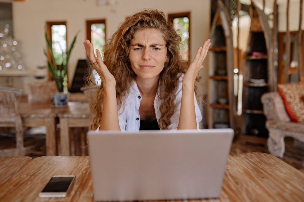 Frustrated woman looking at a laptop screen with hands raised.
